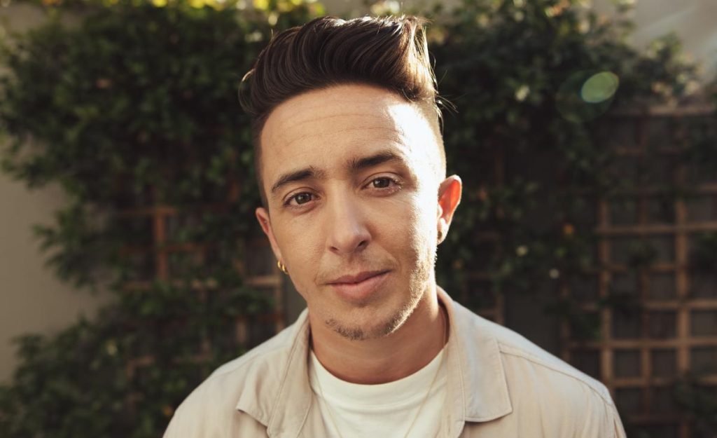 an individual wearing a khaki button up in front of a background of greenery